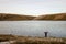 A lone backpacker with arms outstretched standing on the edge of a reservoir looking out on bleak moorland in winter. Elan Valley,