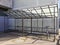 A lone bicycle stands in an indoor bicycle parking area near a gray concrete building on a sunny winter day