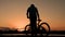 A lone bike stands on the waterfront. A teenager at dawn approaches the bicycle and leaves on it.