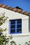 Lone blue window sill on house with white stucco exterior and red adobe roof on home with front yard trees and clear