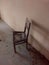 Lone broken chair on tiled floor and near beige colored wall in a empty abandoned dirty house with rubbish and dust on the floor