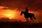 Lone cowboy riding horse silhouetted against a blazing sunset. Generative AI