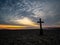 A Lone Cross On A Rocky Beach At Sunrise