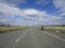 A lone cyclist rides on an asphalt road with road markings in the middle of the fields