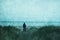 A lone figure, back with camera standing on sand dunes. Looking at the sea on a moody atmospheric day. With a grunge, vintage edit