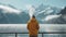 A lone figure stands at a railing back to the camera as they take in the breathtaking view of the mountains and lake