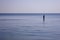 Lone fisherman fishes in a completely calm sea with his feet covered by water. Fishing in relaxing glass calm sea water