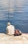 A lone fisherman in a Panama hat sits on a concrete pier with a fishing rod by the water