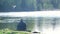 A lone fisherman sits on the bank of a river or lake. Calm and peaceful picture. birds fly over the fisherman