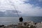 Lone fisherman sitting on rocks at Mediterranean sea beach
