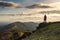 A lone hiker on top of a hill looking out on the ridge of the Malvern Hills, England. On a sunny winters day at sunset