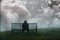 A lone hooded man sitting on a bench in th rain, with a sad, muted, lonely edit