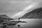 Lone man in landscape image of Wast Water in UK Lake District during moody Spring evening in black and white