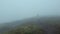 Lone man wanderer walking a hilly road as climbing a mountain in a cold windy day as the wind is blowing clouds and the mist is mo