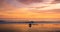 A lone motorcycle and rider driving along a beach at sunset