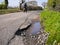 A lone motorcyclist passes unrepaired surface damage to tarmac on a rural road
