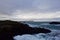 Lone person overlooks ocean from hill above with turbulent seas below