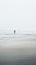 A lone person walking on the beach in the fog, AI