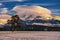 A lone pine tree in the middle of a snowy meadow, in the background a rocky ridge with illuminated dramatic cumulus clouds. Krivan