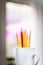 A lone red pencil in front of a group of yellow pencils in a white cup