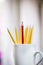 A lone red pencil in front of a group of yellow pencils in a white cup