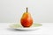 A lone ripe pear on a green plate on a plain white surface and a white background too