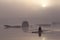 Lone rower on river at misty sunrise