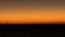 A lone sailboat on the horizon at sunset, its sails glowing orange against the dimming sky