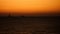 A lone sailboat on the horizon at sunset, its sails glowing orange against the dimming sky