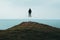 A lone silhouetted, hooded figure floating and dissolving above a hill, looking out across the ocean
