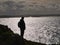 A lone, single female walker, silhouetted against the reflection of the bright sunshine on the sea