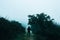 A lone spooky hooded figure standing on a path in the countryside on a foggy, rainy day. With a muted, grainy blue edit