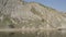 Lone sup surfer moves along calm blue water along mountain rocky shore. Aerial