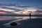 Lone surfer stands on the beach looking out to sea