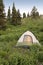 Lone tent pitched on lush green mountain hillside in summer