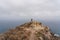 A lone tourist photographer stands on a mountain, against the backdrop of the ocean.