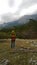 A lone traveller stands on the hill and looks at the mountains. Cloudy dark weather.