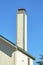 Lone white chimney with slatted wood pannels and dark double gable style roof with decorative blue paint and metal top