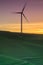 Lone wind turbine spinning on a grassy hillside sunset.