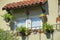 Lone window with adobe red roof tiles on awning with potted plants and decorative balcony on the exterior of house