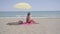 Lone woman sitting on beach under umbrella