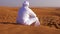 Lonely arab man in white kandura sitting in hot sandy desert