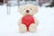 A lonely bear with a big red heart is sitting on the snow waiting. with love on holidays