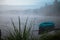 Lonely boat on a peaceful lake. Foggy autumn sunrise twilight. Bright blue turquoise shallop quiet forest, swamp plants