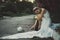 Lonely bride thrown on the wedding day, drinking alcohol from a bottle, sitting on the pavement in a white dress. against the