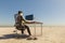 lonely businessman at pc work place in large desert environment remote work and digital nomad and climate crisis concept 3D