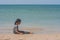 Lonely cute litle girl sitting on sand beach and looking to seascape view.