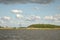 Lonely dead tree in a landscape with water, reeds en bushes under a blue sky, dark clouds coming, Nieuwkoopse Plassen in Holland