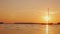 A lonely fishing boat on the mirror surface of the lake. The setting sun illuminates everything with orange light.