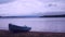 Lonely fishing vessel boat docked on beach at calm lake. Laminate or wooden fishing boat in water